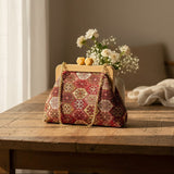 Deep red ornamental tile tapestry bag with honey clasp and a vase of white flowers