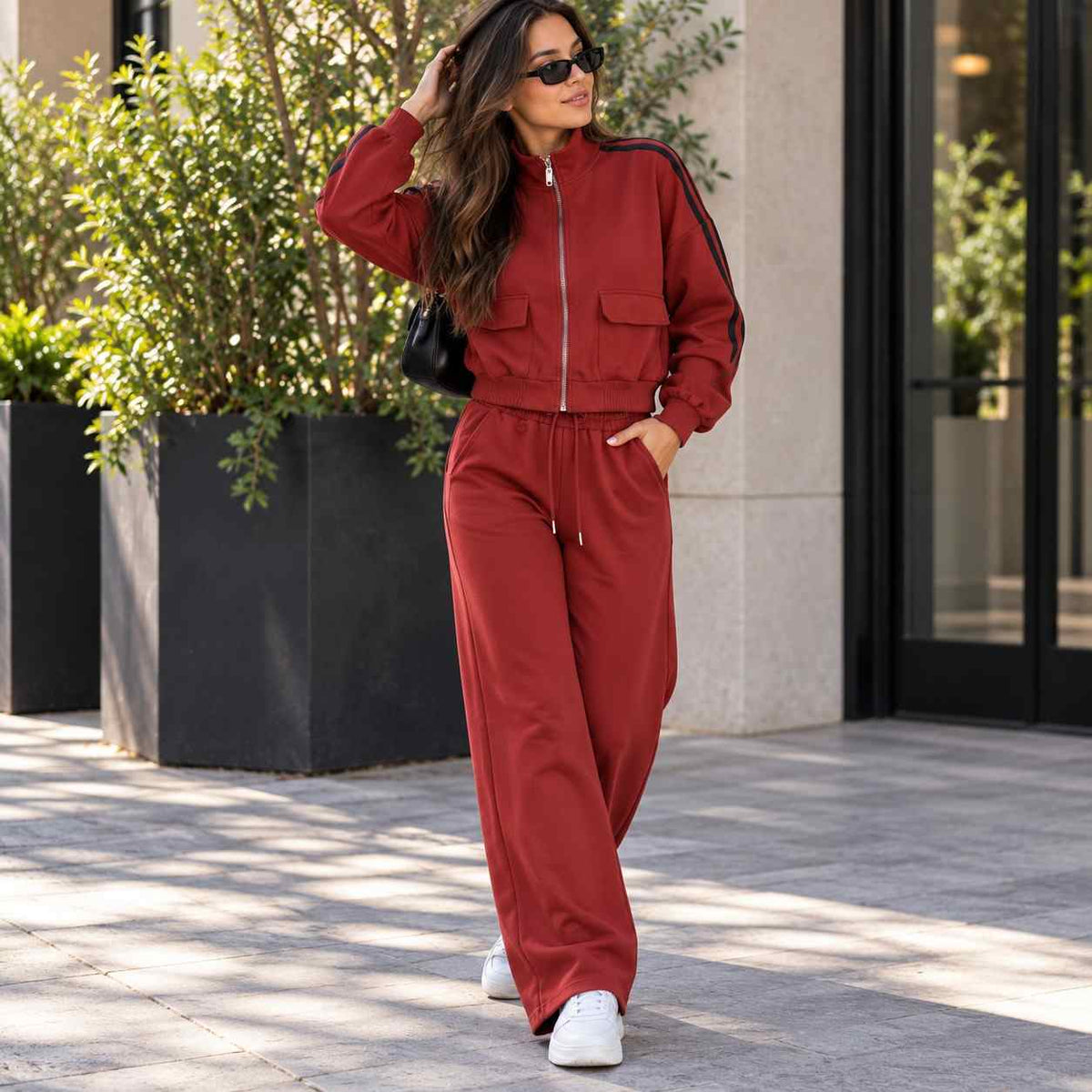 Woman in a red zip jacket with black sleeve stripes and matching wide leg pants on a city street