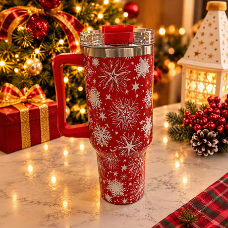 Red insulated tumbler with white snowflake print, red handle and clear lid on a marble table