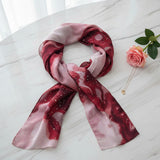 Red and pink patterned sparkly scarf on a white surface with a rose and necklace