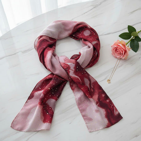 Red and pink patterned sparkly scarf on a white surface with a rose and necklace
