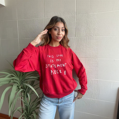 Woman wearing a red crew neck sweatshirt with a white statement piece slogan and light jeans