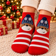 Red and white striped Christmas socks with a brown bear in a navy snowflake beanie by gift boxes