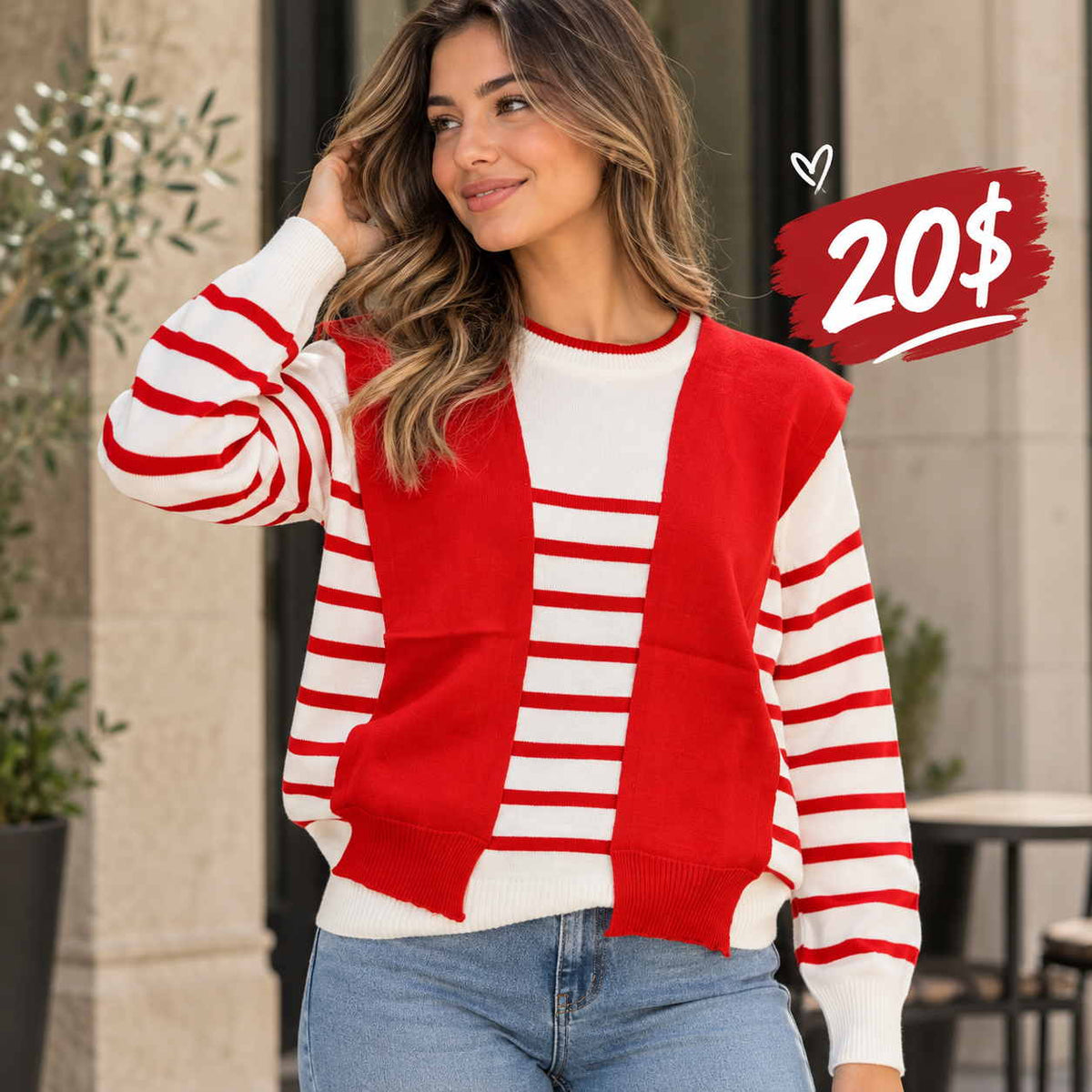 Woman in a white and red striped sweater with an attached red vest layer and blue jeans beside a stone column