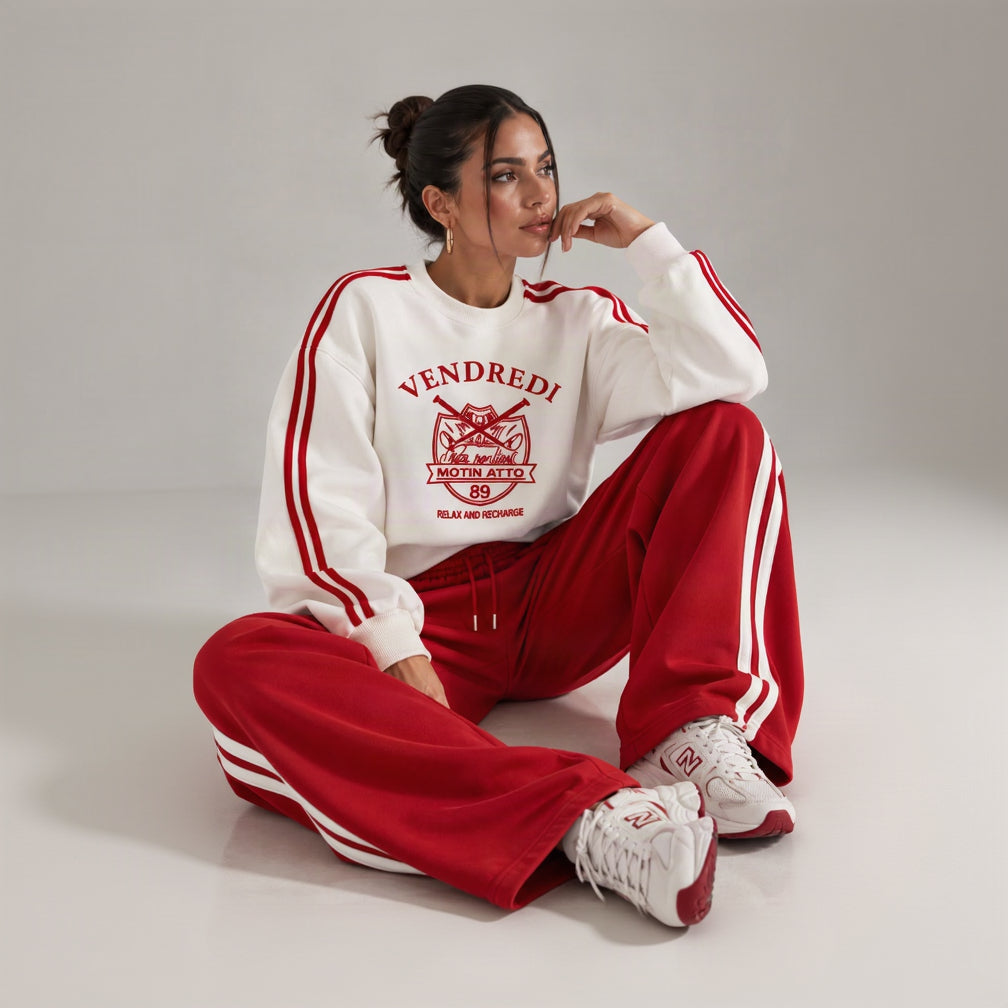 Woman sitting in a red and white varsity print sweatshirt and red wide leg pants with white side stripes
