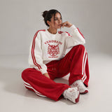 Woman sitting in a red and white varsity print sweatshirt and red wide leg pants with white side stripes