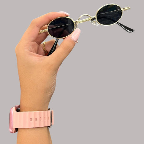 Hand holding a pair of round retro sunglasses with gold frame and black lenses