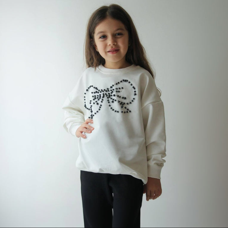 Close up of the beaded rhinestone bow on a cream sweatshirt