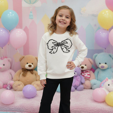 Girl in a cream sweatshirt with a large rhinestone bow and black flared pants