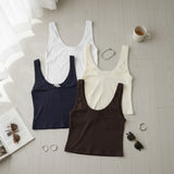 Four ribbed tank tops with wide straps in white, cream, navy and brown laid flat