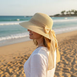 Golden bronze straw sun hat with a long bow trailing down, side profile on the sand