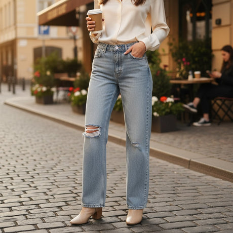 Person wearing light blue ripped jeans standing outside a cafe holding a coffee