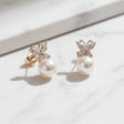 Pair of rose gold butterfly earrings with pearl centers on a light background