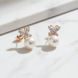 Pair of rose gold butterfly earrings with pearl centers on a light background