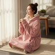 Rose pink hooded blanket with sherpa lined hood and teddy bear embroidery worn seated on a rug