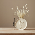 Ceramic vase with dried flowers on a wooden surface against a beige wall