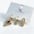 Three gold single earrings on a card with a red stone triangle drop, a mini triangle huggie and a paperclip stud