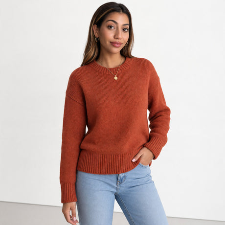 Woman in a rust orange knit crew neck sweater with ribbed hem and cuffs, worn with light blue jeans