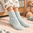 Child wearing sage green cable knit fuzzy socks with teddy bear print pyjamas and a plush bear