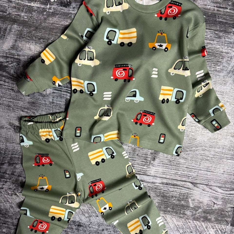 Sage green car print pajama top and pants laid flat on a grey wooden floor
