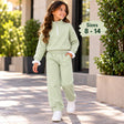 Girl walking in a sage green half zip jogging set with white piping, ruffle cuffs and white sneakers