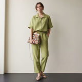 Woman in a sage green outfit holding a colorful bag against a plain background