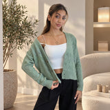 Sage green lace knit cardigan worn open over a white cami with black trousers