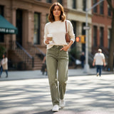 Woman wearing sage green wide jeans walking on a city street holding a coffee cup