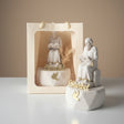 Seated monk statue reading a book beside a cream gift bag holding a second one
