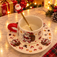White ceramic cup and saucer with Santa prints, red handle and a gold spoon with Santa topper