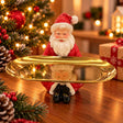 Santa figurine in a red suit holding a long oval golden tray across his lap