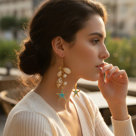 Gold seashell and starfish drop earrings with pearls worn by a woman outdoors