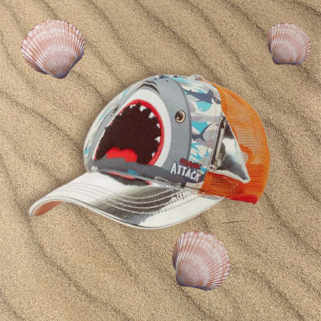 Shark face cap with a white brim and orange mesh back resting on sand beside seashells