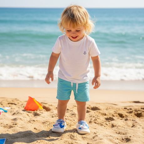 Toddler at the shoreline wearing cream clogs with blue fish faces