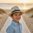 Boy wearing a cream straw fedora sun hat with a navy shark print and navy ribbon band