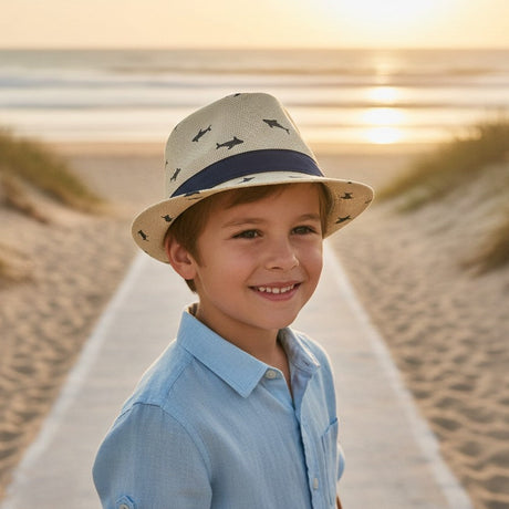 Boy wearing a cream straw fedora sun hat with a navy shark print and navy ribbon band