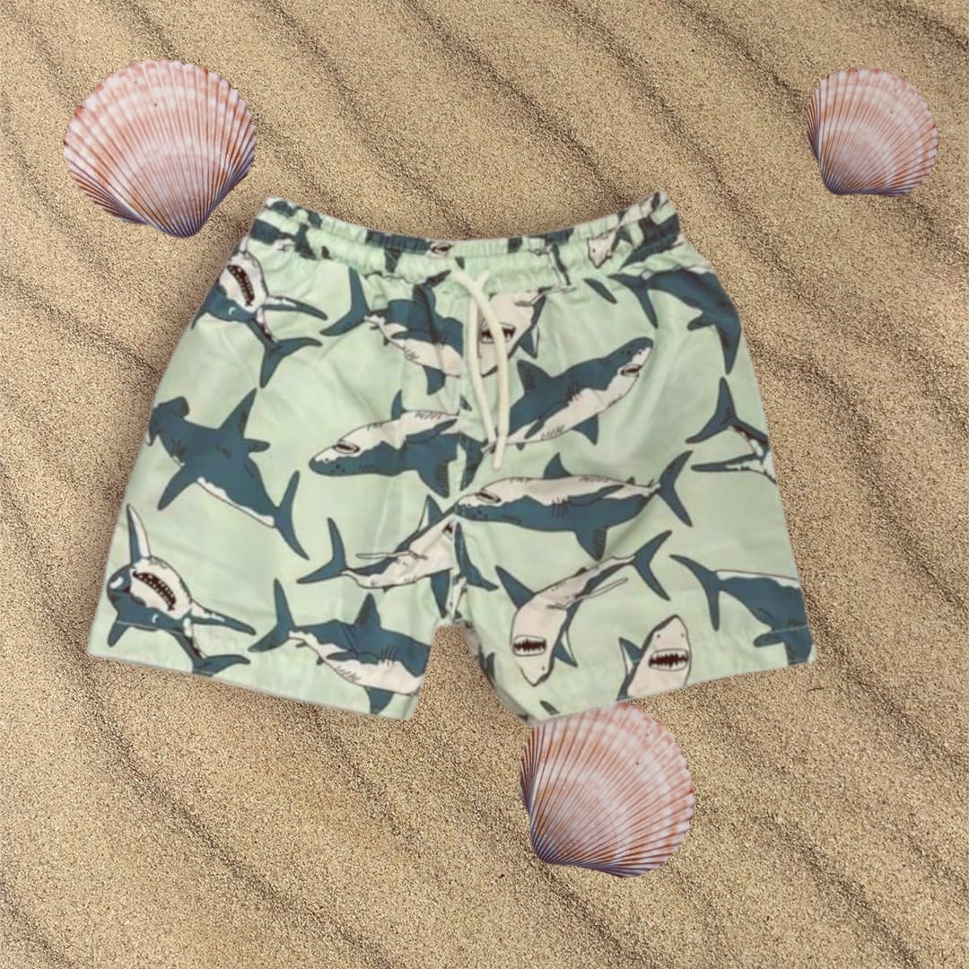 Green Shark-patterned swim shorts on sand with shells