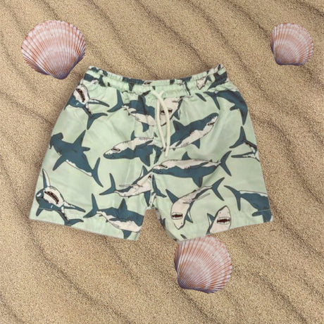 Green Shark-patterned swim shorts on sand with shells