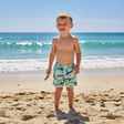Young boy in swim shorts with shark patterns standing on a sandy beach
