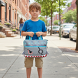 Boy on a pavement holding a grey shark tablet bag with red teeth and blue trim