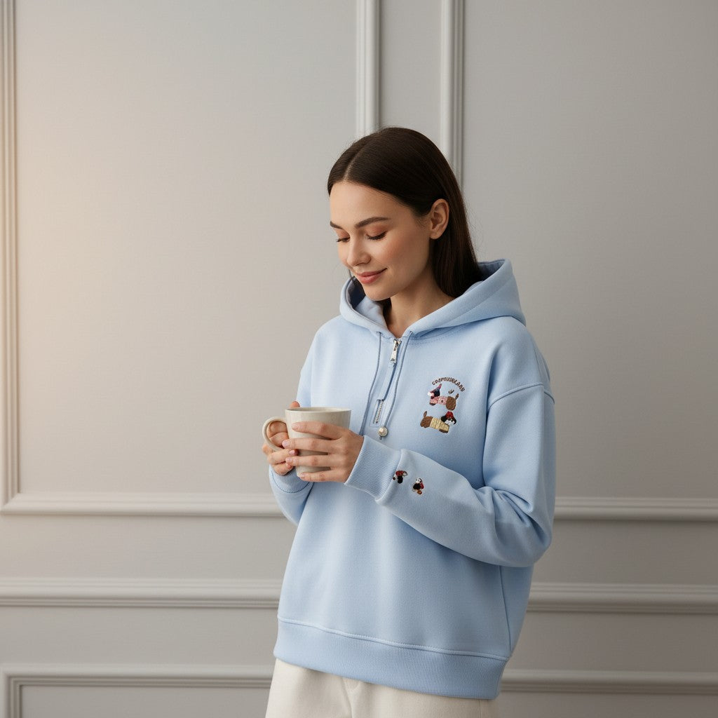 Woman in a light blue hoodie smiling down at her mug against a panelled wall