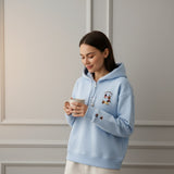 Woman in a light blue hoodie smiling down at her mug against a panelled wall