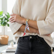 Person wearing a beige sweater and black pants with colorful silk scarf bracelet on a blurred indoor background