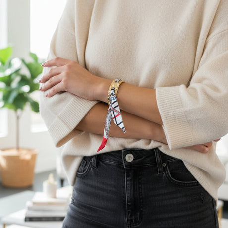 Person wearing a beige sweater and black pants with colorful silk scarf bracelet on a blurred indoor background