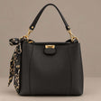 Black top handle bag with gold hardware and a tied scarf on a plain grey background