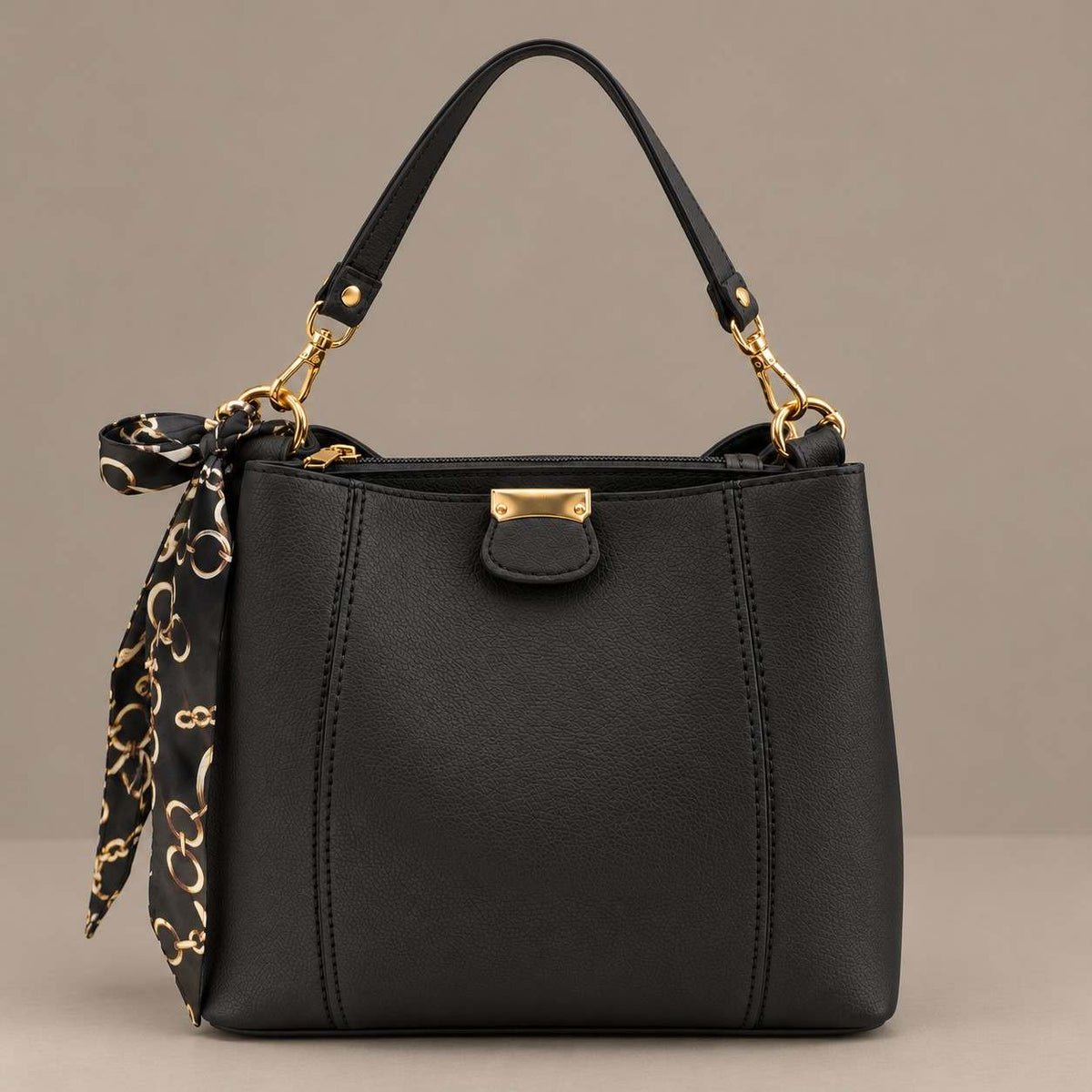 Black top handle bag with gold hardware and a tied scarf on a plain grey background