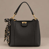 Black top handle bag with gold hardware and a tied scarf on a plain grey background