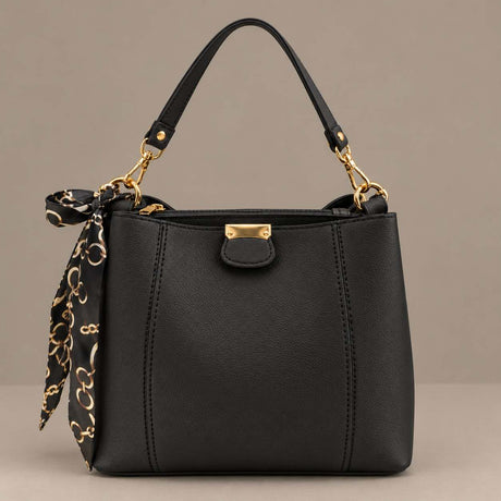 Black top handle bag with gold hardware and a tied scarf on a plain grey background