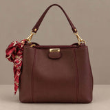 Burgundy top handle bag with gold clips and a printed scarf tied at the side
