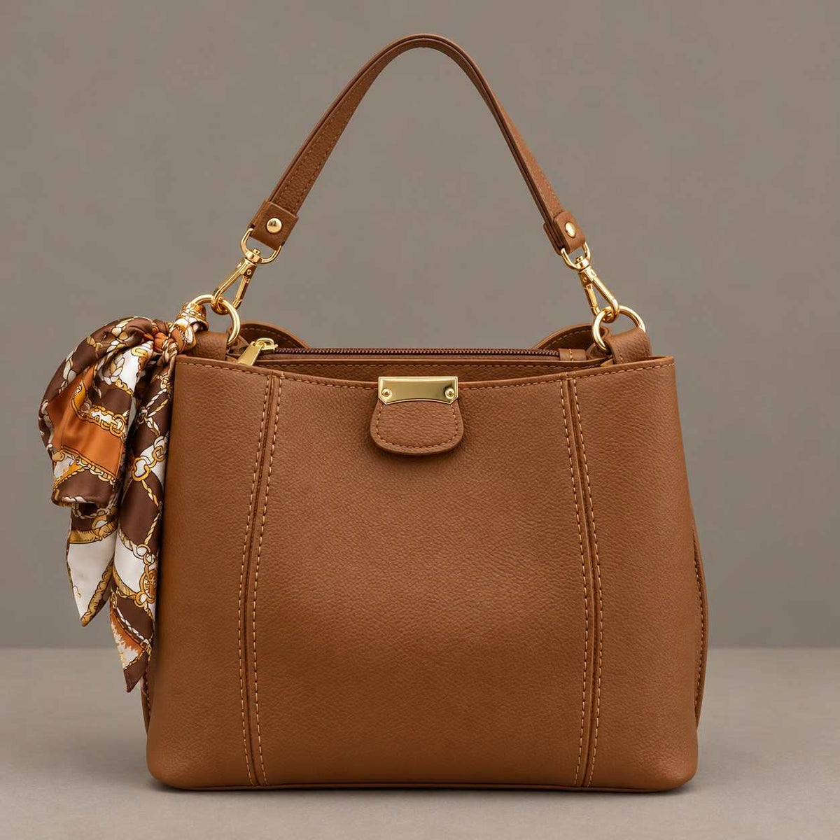 Camel top handle bag with a gold front plate and an orange and cream print scarf